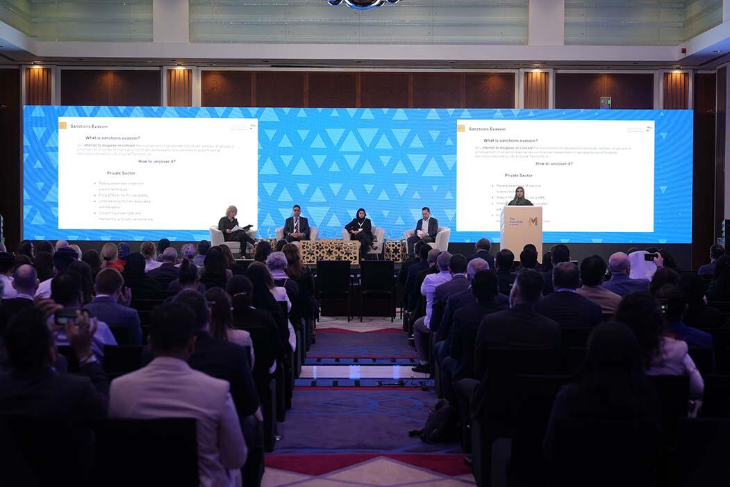 A large audience attentively watches a presentation during a conference, engaged in the speaker's insights.