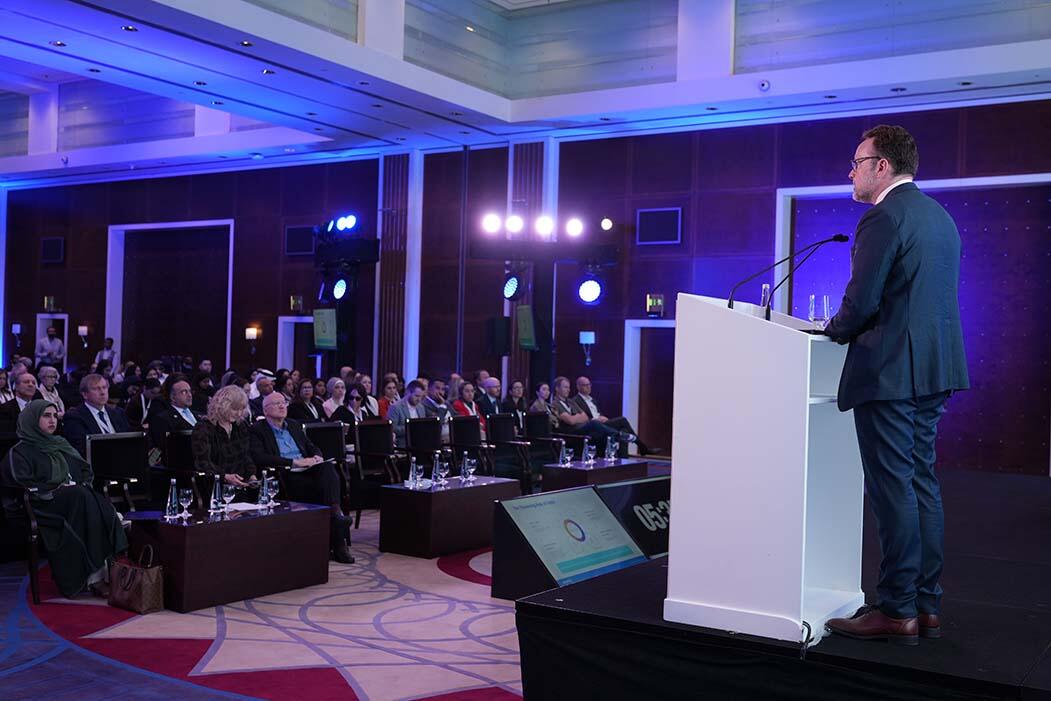 A man in a suit delivers a speech at a conference, engaging the audience with his presentation.