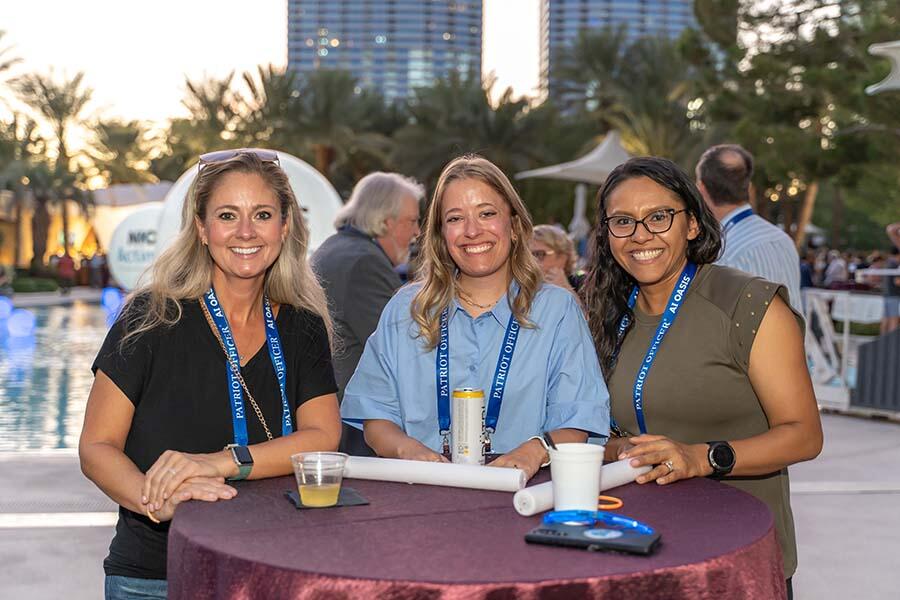 Three women smiling at the camera, capturing a joyful moment at a lively event.
