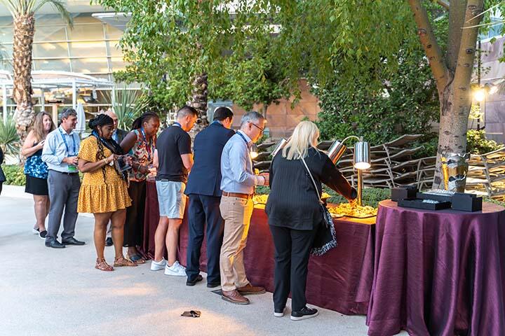 A group of people gathered around a table filled with various food and drinks, enjoying a social gathering.