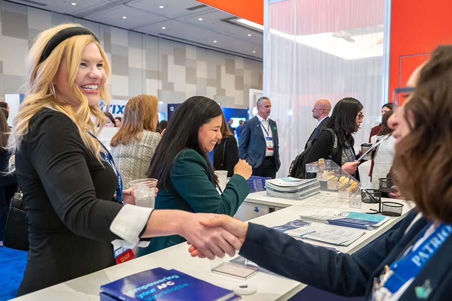 A woman and another woman shake hands at a trade show, symbolizing networking and professional collaboration.