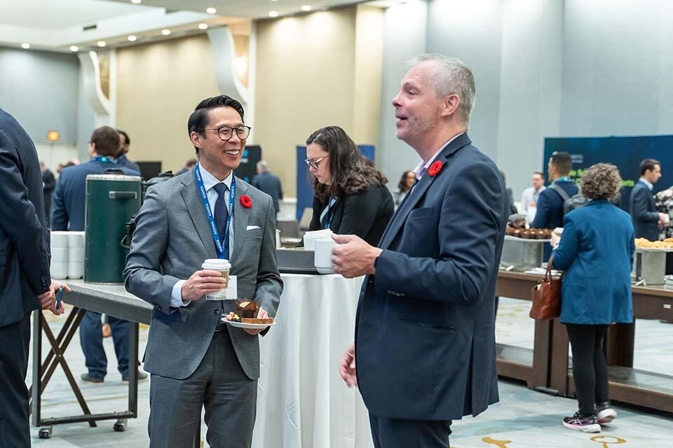 Two men in suits and ties engaged in conversation at a professional conference setting.