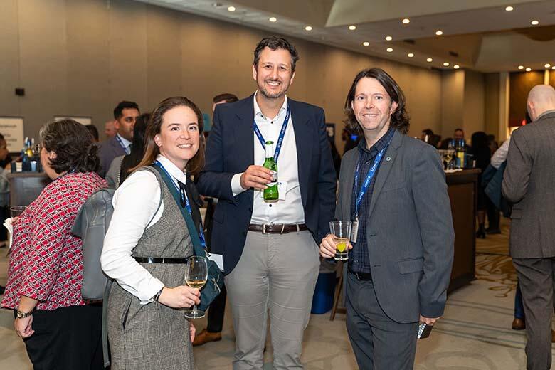 Three professionals networking at a business event, each holding a drink and engaged in conversation.