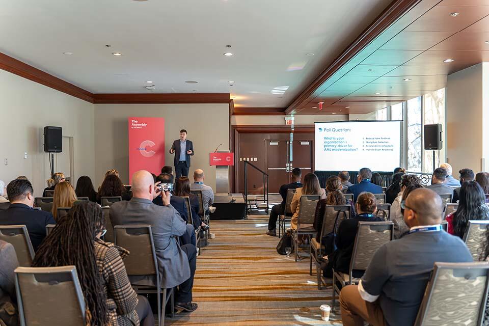 A man stands confidently at a podium, presenting to a captivated audience in a spacious conference hall.