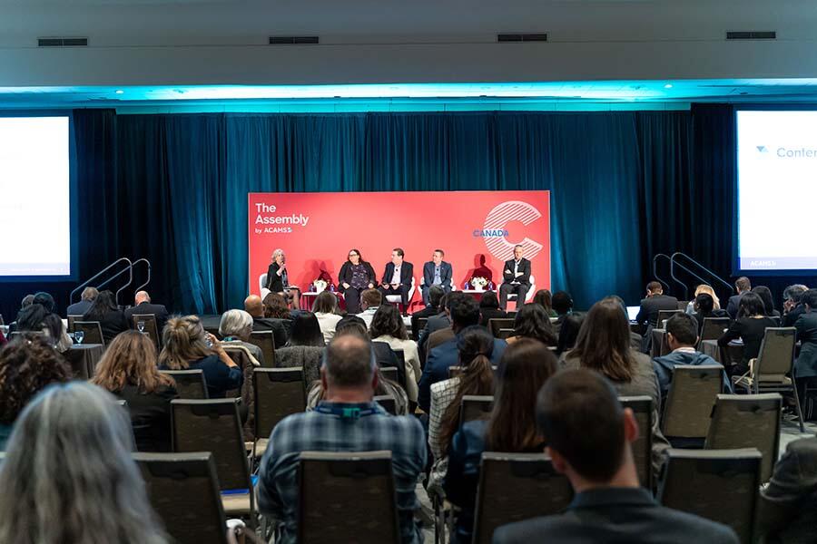 A diverse group of individuals seated in chairs, engaged in discussion at a professional conference setting.